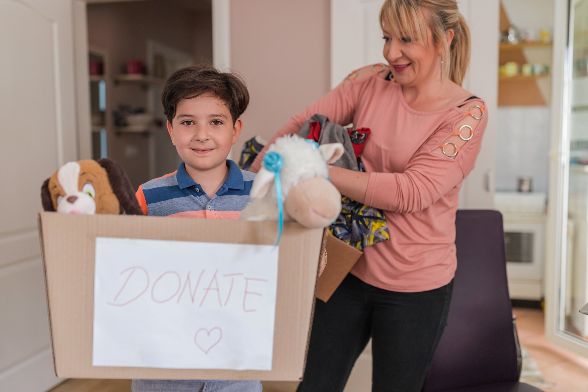 Happy woman observing her son holding box of his toys ready for donations